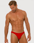 Man wearing the Luné d’Or Forme Men’s Thong in red, front view showing the contoured pouch and slim waistband.